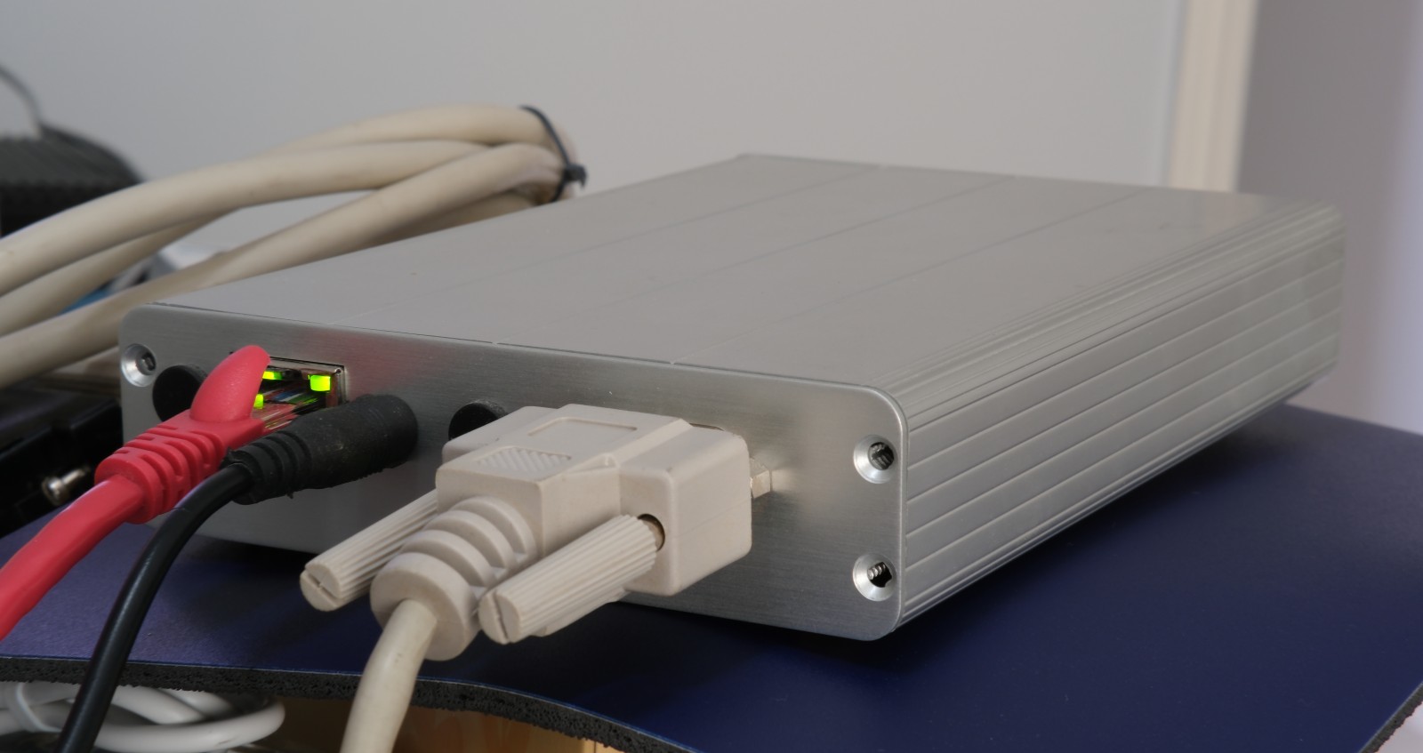 Photo of alix3d2 in aluminum case. It's longer than it is wide, kinda like a modem. It has power, Ethernet, and DB-9 serial cables connected.