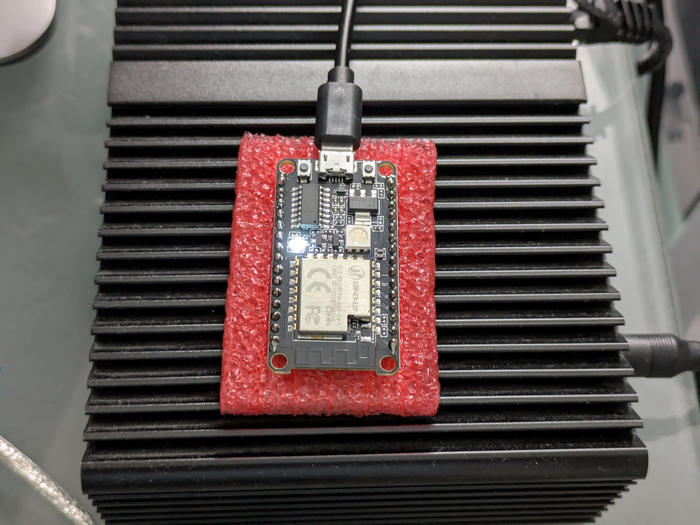 Photo of a ESP32-C3 dev board sitting in red foam with a USB cable attached. A white LED on it is illuminated