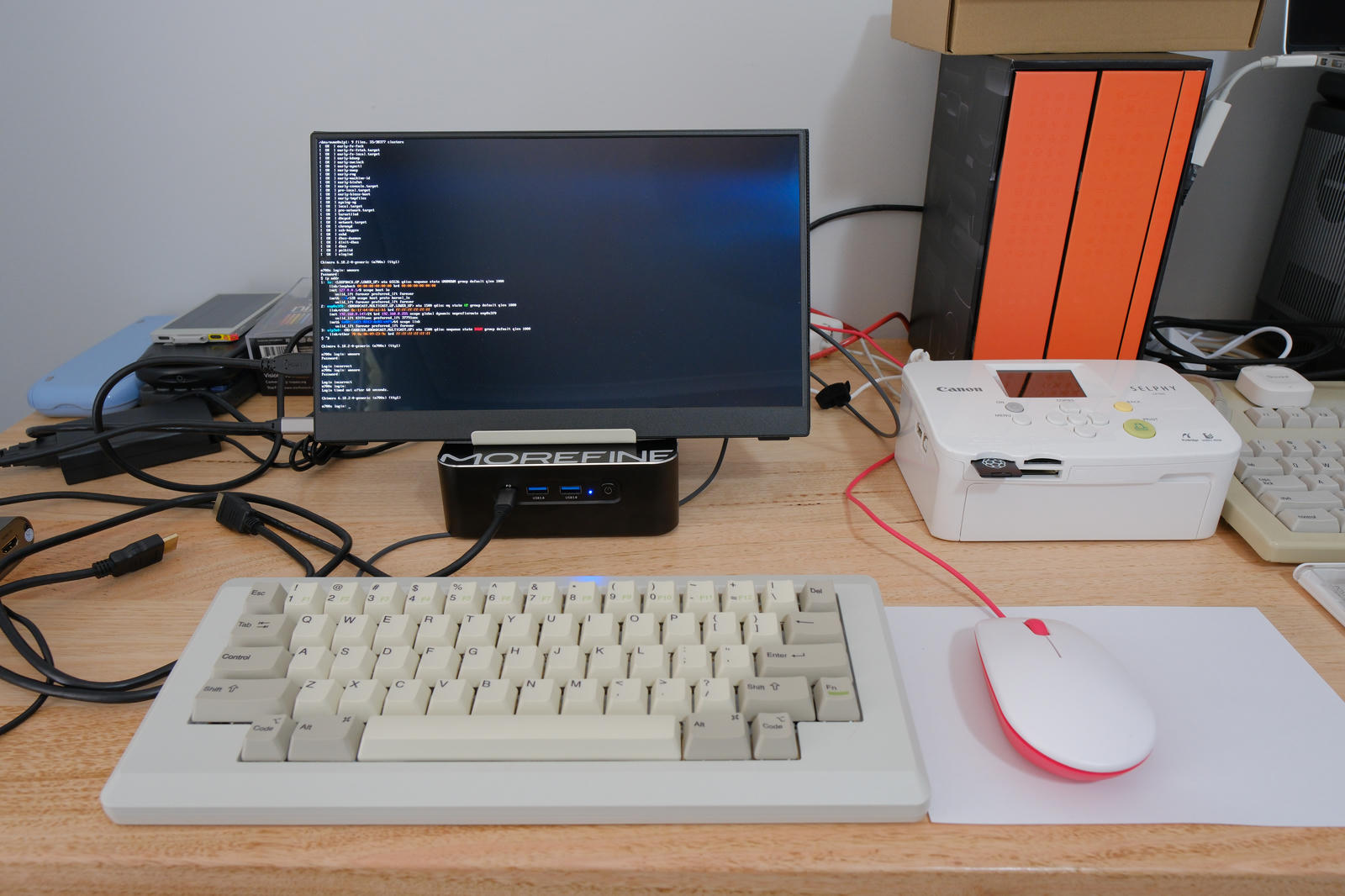 MOREFINE on wooden desktop with portable LCD on top. In front is a mechanical keyboard styled after the keyboard on the original Macintosh and a red and white Raspberry Pi mouse.