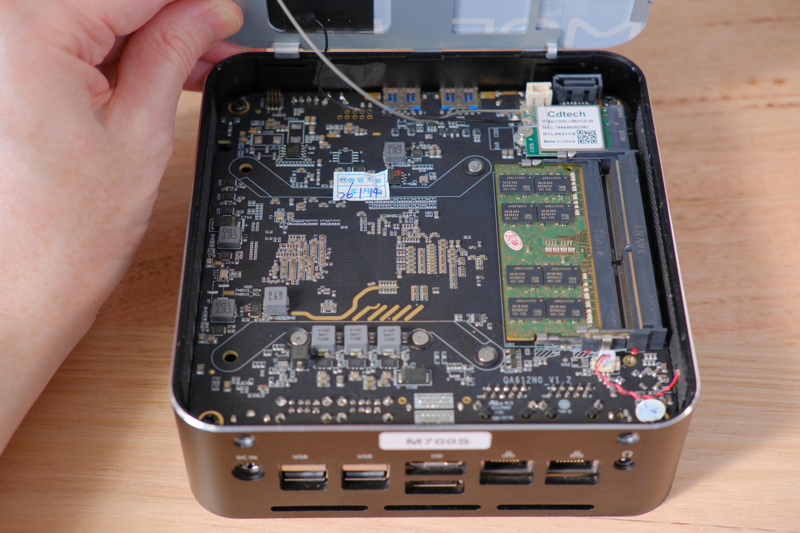 M700S with top lid flipped up and being held in place with my hand. Inside is a circuit board filling the space. On the right is a double-decker SO-DIMM RAM slot with one slot populated.